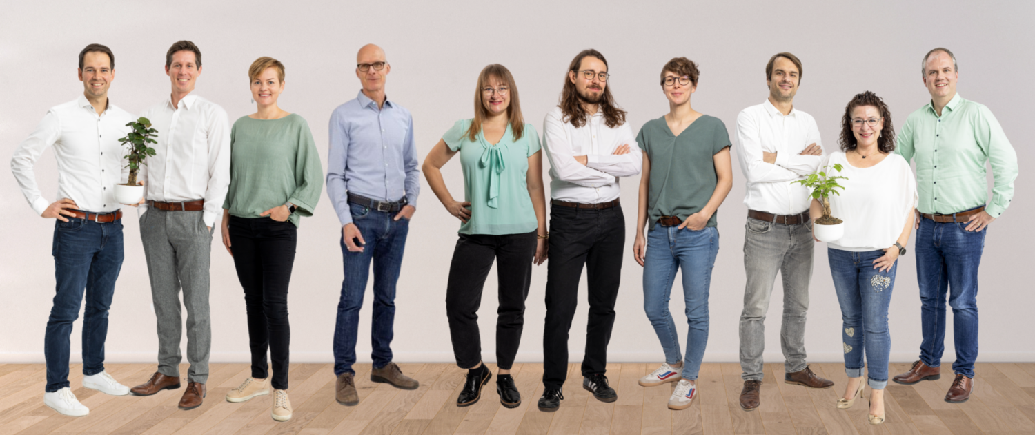Gruppenbild des Klimapartner Teams, die Mitarbeitenden stehen lächelnd vor einer beigen Wand